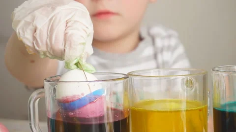 Close-up child holding an egg with one hand and dropping it into a glass of Stock Footage 120347799