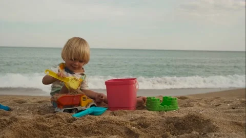 Close-up of a child playing with a shovel and bucket on the sand at the beach Stock Footage 220732433