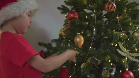 Close-up child red Santa hat decorates Christmas tree beautiful bright balls Stock Footage 250488098