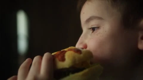 Close up of a child taking a bite of a homemade burger with fresh lettuce and a Vídeos de archivo 340524405