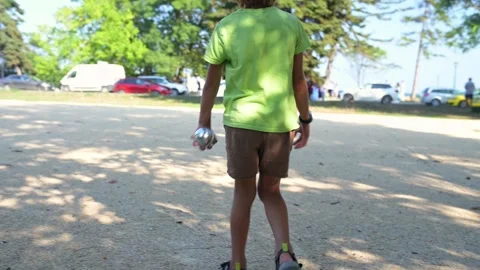 Close-up of a child throwing a petanque ball, in a sunny park. The image Stock Footage 284037133