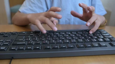 Close-up of child typing on computer keyboard at wooden desk. Concept of Stock Footage 316097837