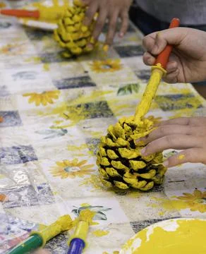 Close up of children hands decorating pine cones with yellow paint Stock Photos