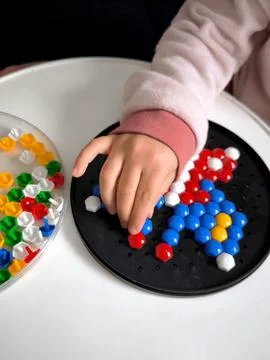 Close-up of a childs hand busy assembling a hexagonal mosaic on a round black 스톡 사진
