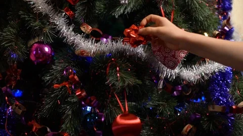 Close-up of the child's hand hangs puts a red Christmas tree toy bow on the Chri Stock Footage 122031664