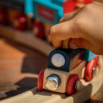 Close-up of child's hand playing in the sun with a wooden toy train Stock Photos