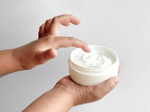 Close up of childs hands holding container of hand cream and dipping finger on Stock-Fotos