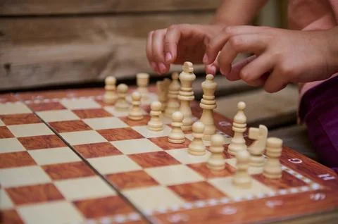 Close-up of child's hands setting up chess pieces on a wooden chessboard, f.. Stock Photos