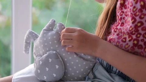 Close-up of a child's hands sewing a soft toy near the window. Stock Footage 217960637