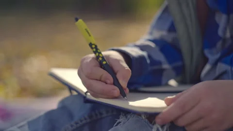 Close-up of a child's hands writing in a notebook in an autumn park. Stock Footage 256093047
