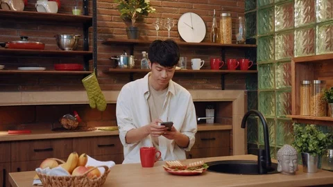 Close up chinese young man on kitchen use phone at home drink tea business house Stock Footage 108123477