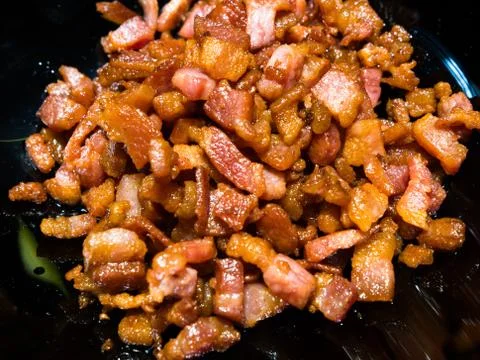 Close-up on chopped, crispy fried bacon on black background. Stock Photos
