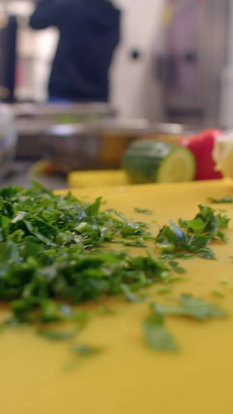 Close-up of chopped green herbs on yellow cutting board in commercial kitchen 库存影片 336534314
