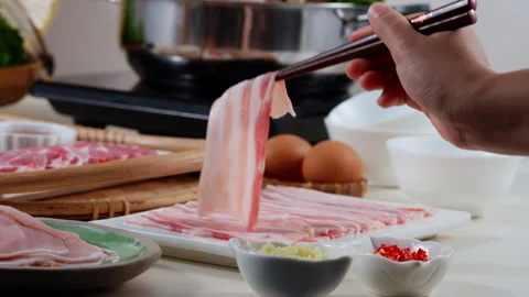 Close-up of chopsticks laying down a raw bacon slice on a grill, showcasing the Stock Footage 285038081
