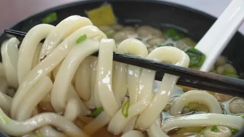 Close-Up of Chopsticks Lifting Thick Udon Noodles from Savory Dashi Broth Stock Footage 333527223