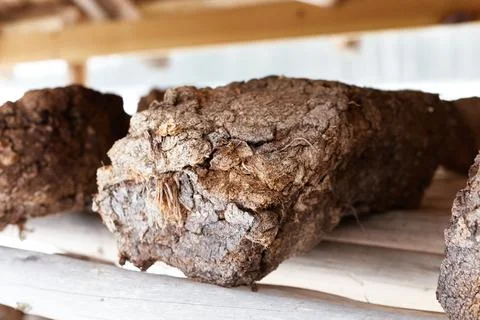 Close up chunk of peat between others piled up for drying on wooden shelf. Pe Stock Photos