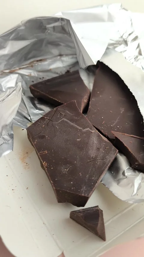 Close-up chunks of dark natural chocolate in foil packaging Video stock 324555100
