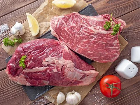 Close-up of chunks of juicy raw beef on parchment. Vegetables and spices arou Stock Photos