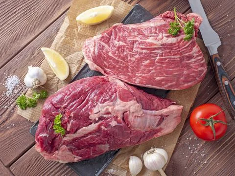 Close-up of chunks of juicy raw beef on parchment. Vegetables and spices arou Stock Photos