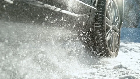 CLOSE UP: Chunks of snow fly in the air as car tries to start on a snowy road. Stock Footage 145648163