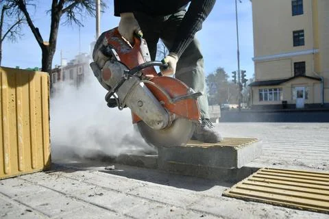 Close-up of a circular saw as a worker cuts a road curb. 스톡 사진