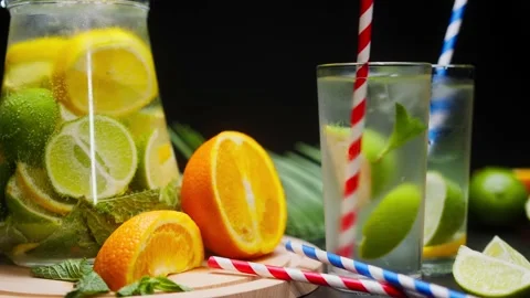 Close-up of citrus fruit drinks in jug and glasses, mixing with a straw a Stock Footage 155117464