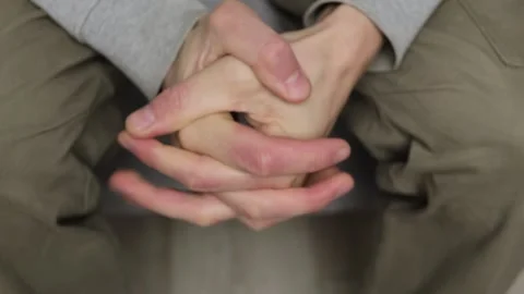 Close-up of clasped hands resting on knees, showing tension and stress in a Stock Footage 296221432