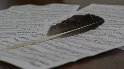 Close-up of classical music sheet pages scattered on wooden table with feather Stock Footage 307783134