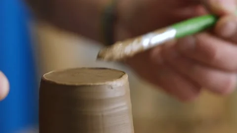 Close-up, a clay cup rotates on a potter's wheel. a brush smears clay parts.  Stock Footage 144244892