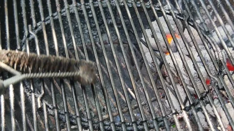 Close-up cleaning a hot portable BBQ grill with a brush removing old fat an.. Stock Footage 337410199