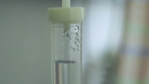 Close-up of Clear Liquid Bubbles Rising in Medical IV Drip Chamber Видео 339072999