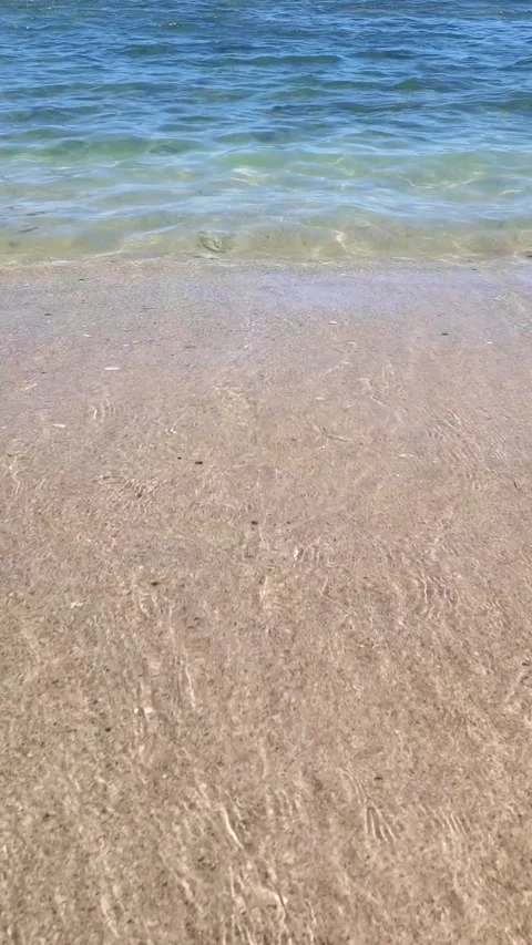Close up of clear ocean waves washing onto a sandy beach on a sunny day Stock Footage 336339239