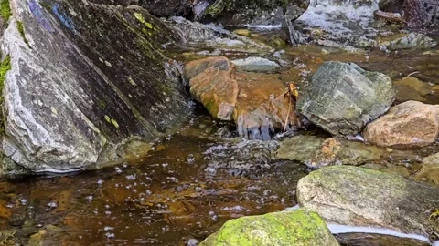 Close up of clear water cascading over smooth grey and rusty orange stones Stock Footage 345168183