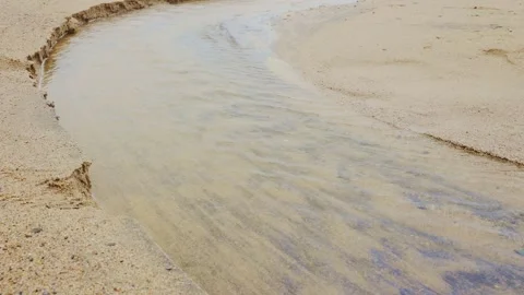 Close-up of clear water stream flowing over fine sand on a beach Stock Footage 338194051