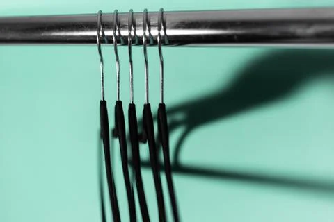 Close-up of clothes rack with black empty hangers on background of aqua menthe. Stock Photos