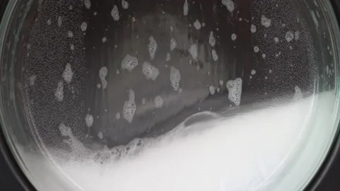 Close up clothes in washing machine with bubbles foam soap in laundromat shop Stock Footage 221919612