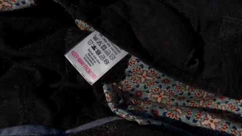 Close up of clothing care on dark patterned fabric with folded textile texture Stock Footage 345608734
