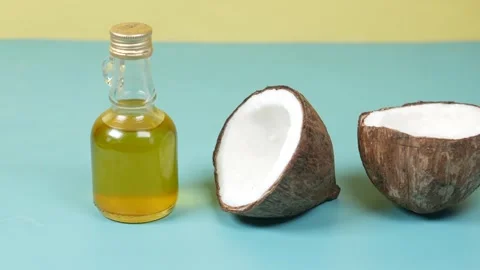 Close up of coconut oil in a small bottle next to a halved coconut on blue .. Vídeos de archivo 332626532