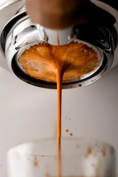 Close-up of coffee being brewed by machine flowing through portafilter into Stock Photos