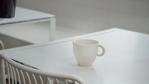 Close-up of coffee being poured into a white Cup on a white table from a glass Stock Footage 131064713