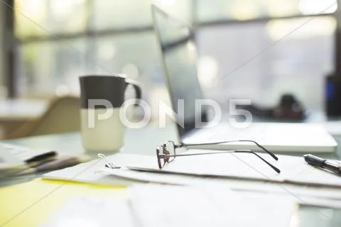 Close Up Of Coffee Cup And Eyeglasses On Paperwork Near Laptop