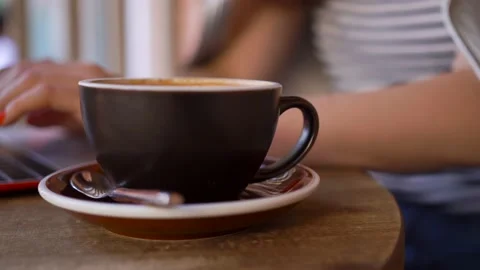 Close-up coffee cup, background blurry girl prints on laptop, takes a coffee sip Stock Footage 137564450
