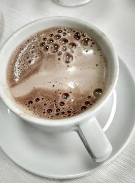 Close-up of coffee cup with frothy surface and bubbles on white saucer, sof.. Stock Photos