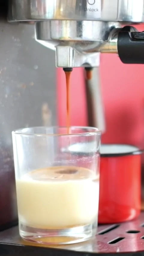 Close-up of a coffee machine pouring hot espresso into a glass with sweetened Stock Footage 344785643