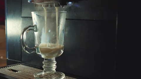 Close-up of a coffee maker dispensing a warm latte into a glass cup Stock Footage 346472048