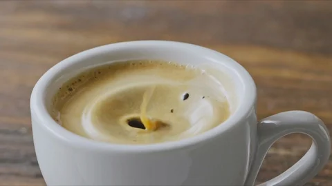 Close-up of coffee splashes fall into a cup of espresso with froth on a brown Stock Footage 129636463
