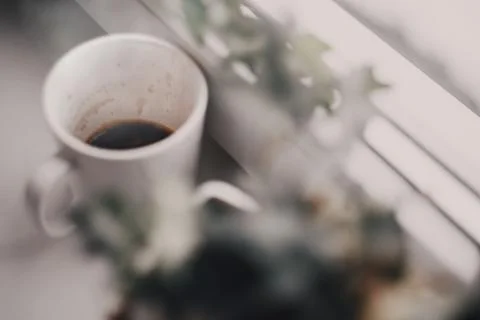 Close-up of coffee in a white mug next to green foliage on a windowsill in .. Stock Photos