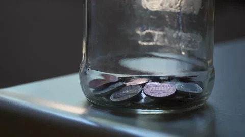 Close-up of coins falling into the bottom of a glass jar Vídeos de archivo 320189998