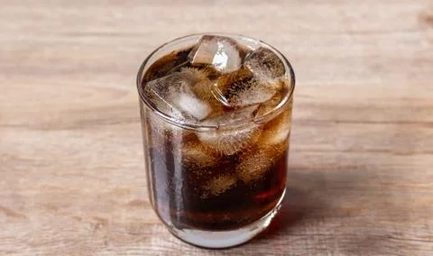 Close up cola and ice cube in clear glass on wooden table Stock Photos