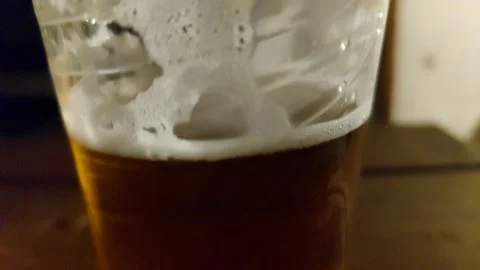 Close-up of a cold beer with white foam bubbles inside a transparent plastic cup Stock Footage 335474962